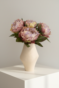 Dusty pink and lavender silk peonies arranged in a cream ribbed vase
