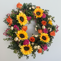 Summer silk flower wreath with sunflowers, orange and pink roses and green foliage on a cream background
