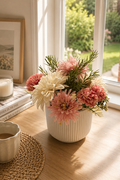 Floral arrangement in a white vase on a windowsill with a cup of coffee and books.